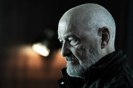 A high-definition desktop wallpaper featuring a somber-looking character from The Walking Dead: The Ones Who Live, with a shadowy, dramatic backdrop.