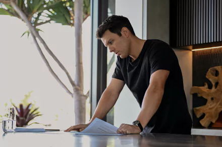 HD Wallpaper featuring a scene from the TV show Apples Never Fall with a focused man reviewing documents at a modern desk.