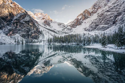 A serene frozen lake reflects majestic snow-capped mountains, surrounded by evergreen trees, creating a stunning winter landscape in high-definition.