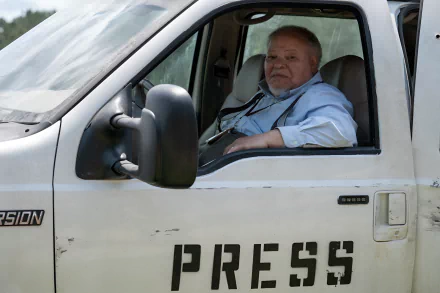 A man sitting in the driver's seat of a white vehicle with the word PRESS on the door, possibly portraying a character in a movie related to a Civil War theme. The image serves as a high-definition desktop wallpaper.