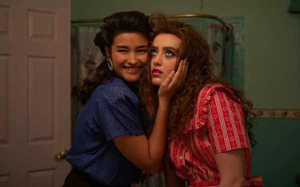 Two young women share a playful moment in a bathroom, showcasing 1950s-inspired fashion. This HD wallpaper features a scene from the movie Lisa Frankenstein.