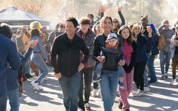 HD desktop wallpaper featuring a scene from the movie The Family Plan with smiling people at an outdoor event.
