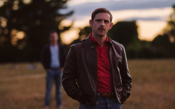 HD desktop wallpaper featuring a contemplative man in the foreground from the movie 'All of Us Are Strangers' with another figure blurred in the background, set in a dusky field.