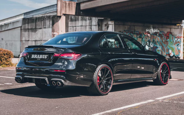 A sleek Brabus 800 E63 parked under a bridge, showcasing its striking design and bold red accents, set against an urban backdrop with graffiti art. HD desktop wallpaper.