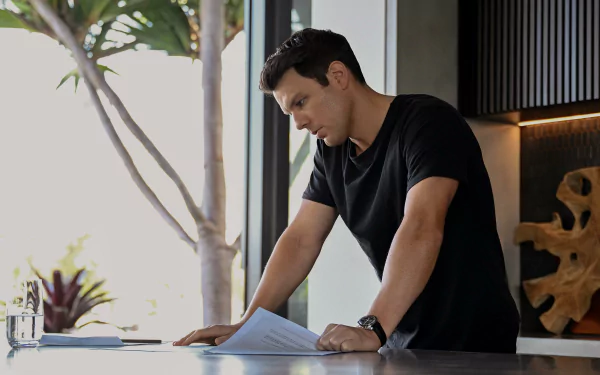 HD Wallpaper featuring a scene from the TV show Apples Never Fall with a focused man reviewing documents at a modern desk.