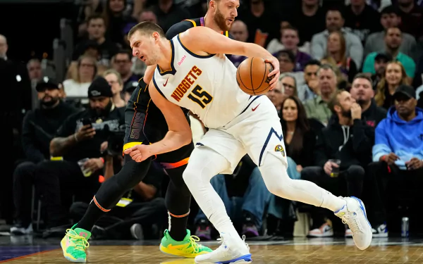 Nikola Jokić of the Denver Nuggets dribbles the basketball during an NBA game, showcasing his skill amidst a lively crowd. HD wallpaper capturing a dynamic moment in basketball.