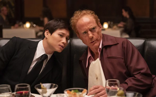 HD wallpaper featuring two characters from the TV show The Sympathizer, a young man in a suit and an older man in a maroon shirt, leaning closely together at a restaurant, possibly engaged in an intense conversation.