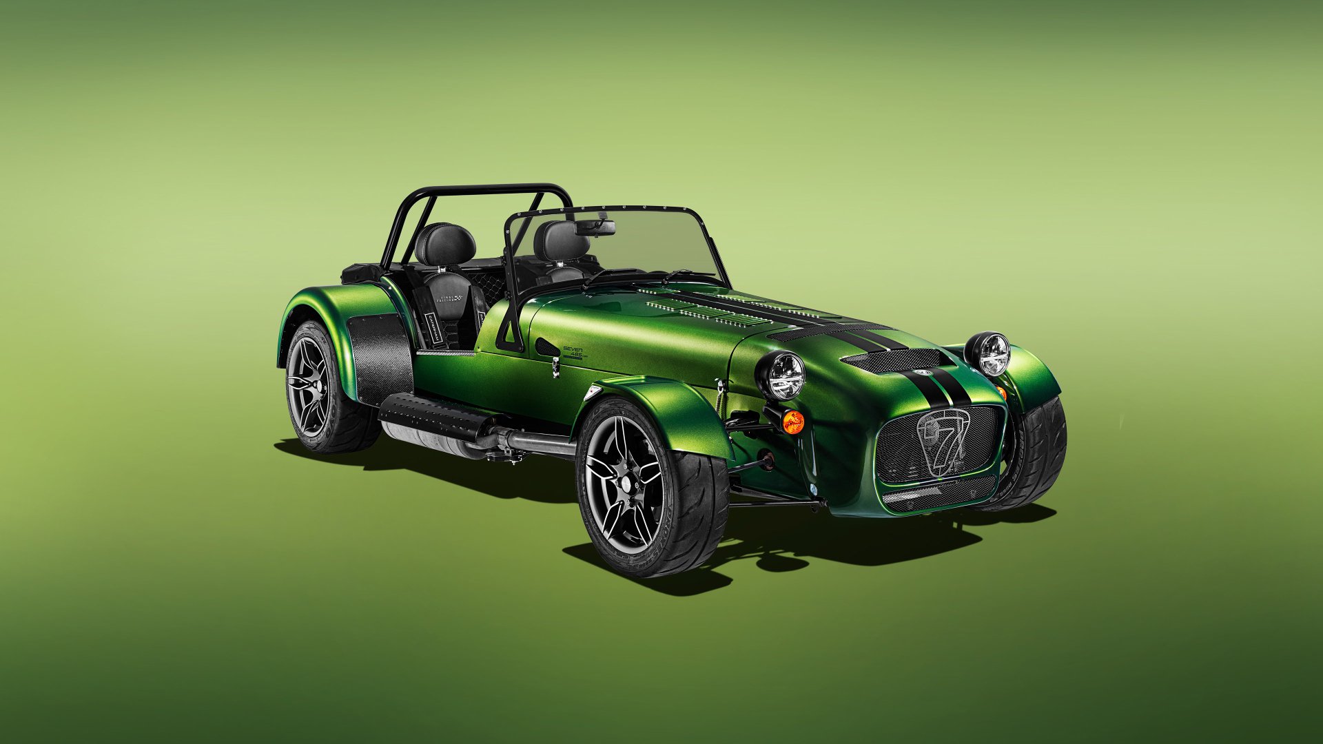 A high-definition desktop wallpaper featuring a green Caterham Seven 485 sports car on a smooth gradient green background.