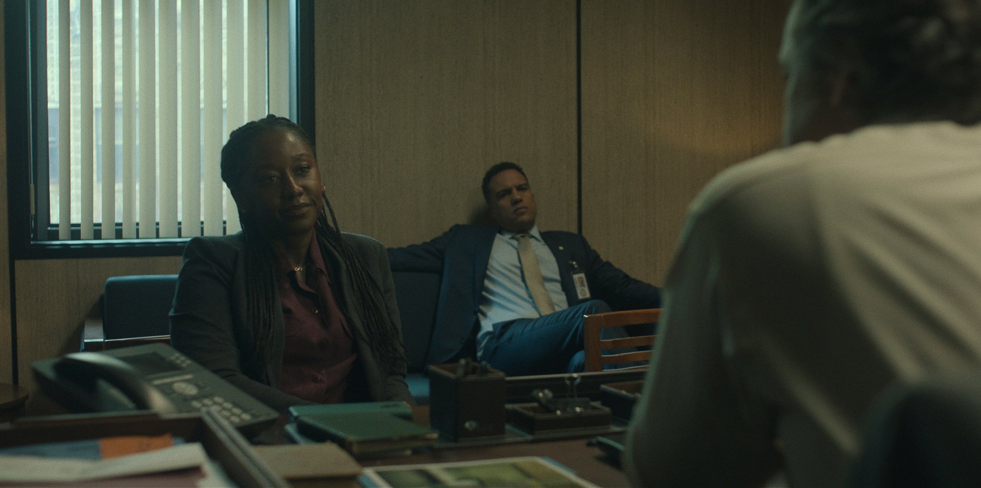 Scene from the TV show Presumed Innocent (2024) showing three people in a dimly lit office, with two sitting opposite another. The image is an HD desktop wallpaper and background.