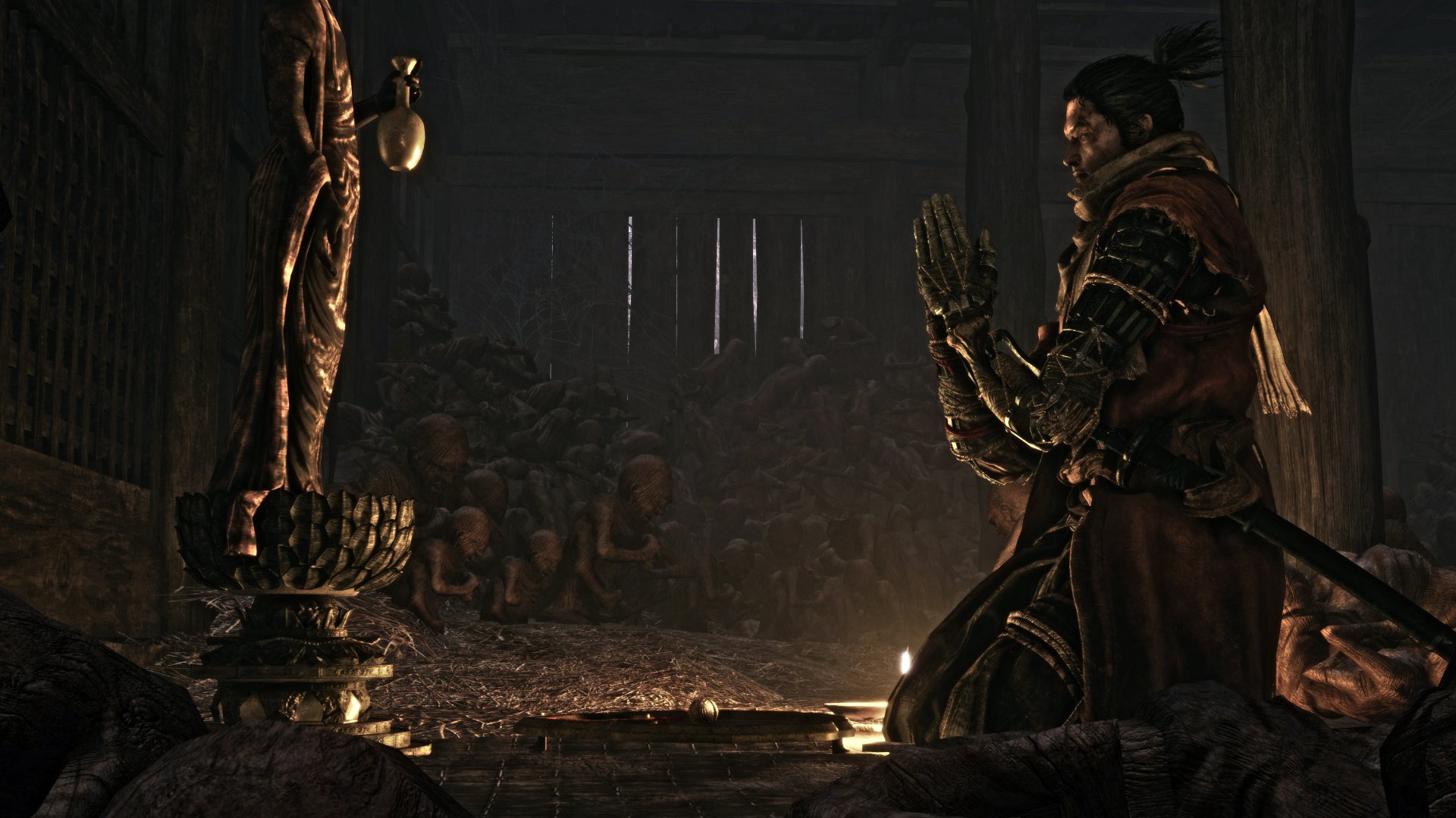 Sekiro kneels in prayer before a statue in a dark, mysterious setting from the game Sekiro: Shadows Die Twice. This HD desktop wallpaper captures the game's atmospheric and immersive world.