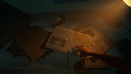 A hand reaches for scattered newspapers under dim lighting in a scene from the video game The Bridge Curse 2: The Extrication. This HD desktop wallpaper evokes a mysterious and eerie atmosphere.