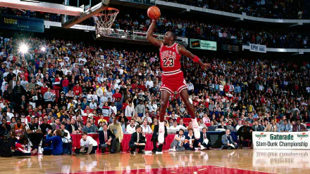 HD wallpaper of Michael Jordan in a Chicago Bulls jersey performing a slam dunk in an NBA game, with a crowded stadium in the background.