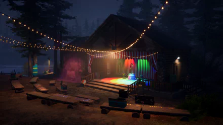 HD desktop wallpaper of Killer Klowns from Outer Space: The Game, featuring a spooky nighttime scene with a lit stage, string lights, and scattered seating in a wooded area.