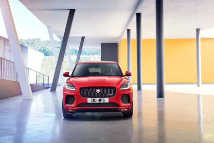HD desktop wallpaper featuring a front view of a bright red Jaguar E-Pace parked in a modern architectural setting with tall columns and a yellow accent wall in the background.