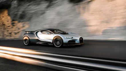 HD desktop wallpaper featuring a sleek silver Bugatti Tourbillon speeding along a blurred road with a rocky background.