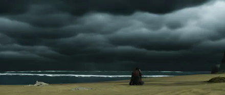 HD PC desktop wallpaper from Ghost of Tsushima featuring a lone warrior kneeling on a beach under ominous, dark clouds by the ocean.