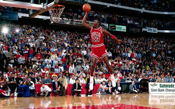 HD wallpaper of Michael Jordan in a Chicago Bulls jersey performing a slam dunk in an NBA game, with a crowded stadium in the background.