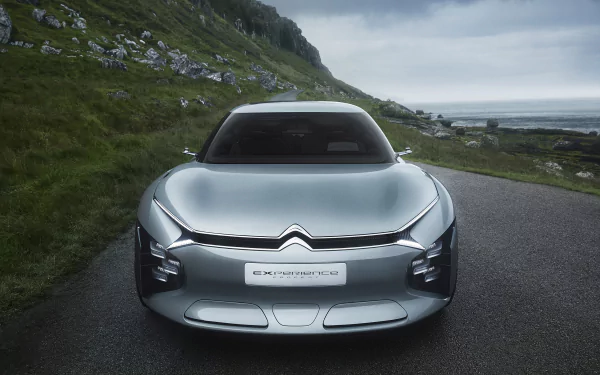 HD desktop wallpaper of a Citroën CXperience, featuring the car on a scenic road with green hills and a cloudy sky in the background.