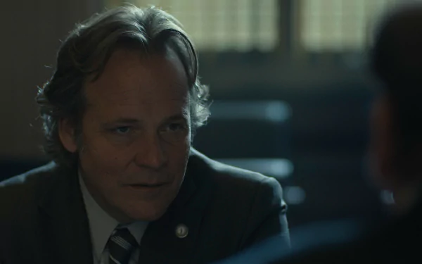 HD desktop wallpaper featuring Peter Sarsgaard in a scene from the TV show Presumed Innocent (2024). The image captures a contemplative moment with a blurred background adding depth to the setting.