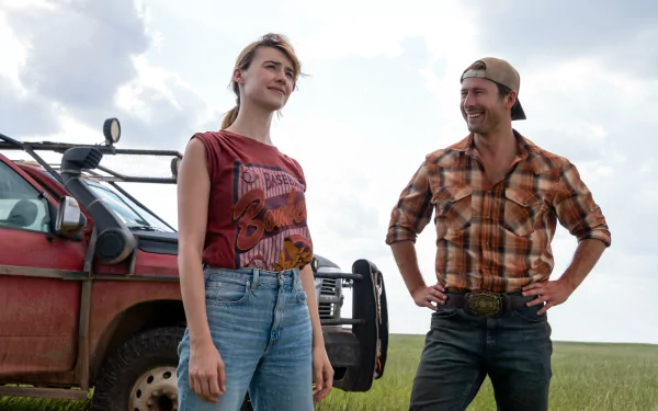 HD desktop wallpaper from the movie Twisters featuring Glen Powell and Daisy Edgar-Jones standing outdoors in casual attire, with a red vehicle in the background.