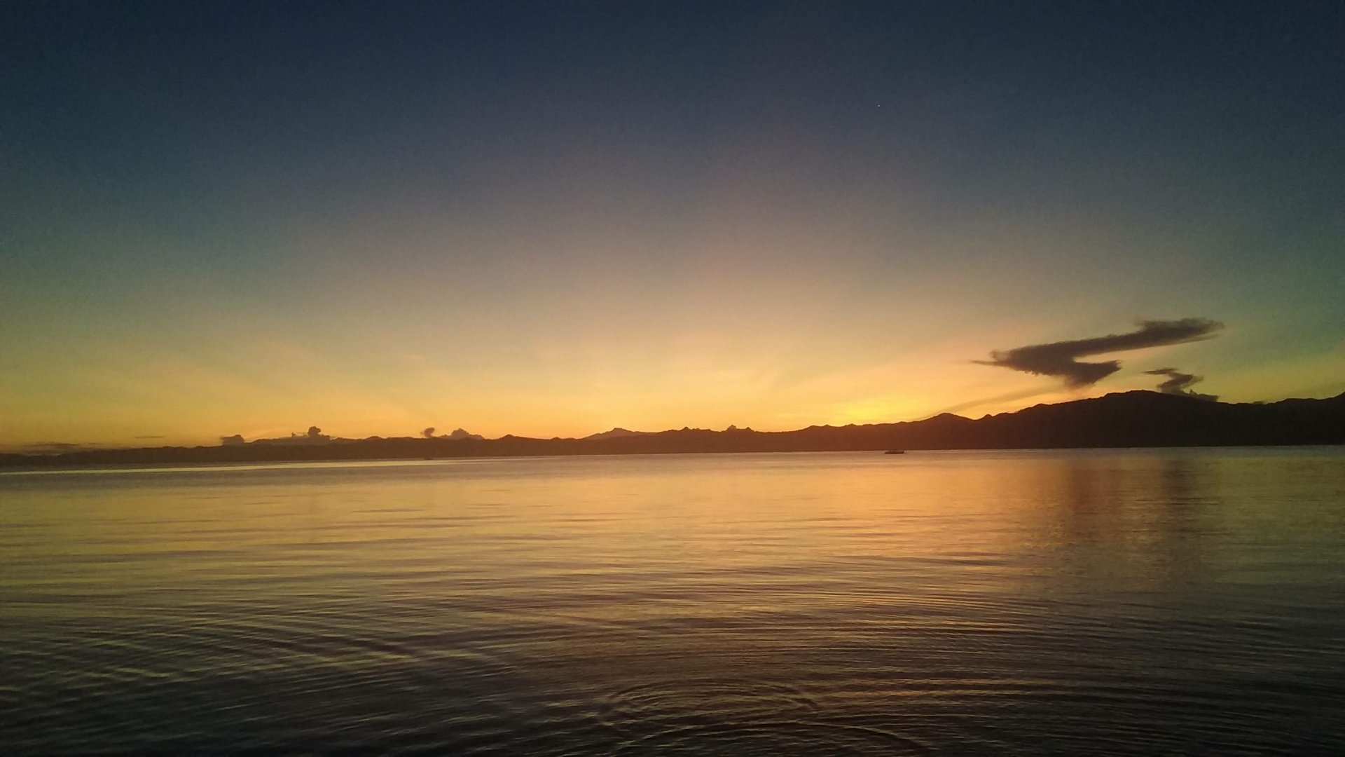 HD PC desktop wallpaper of a serene beach at sunrise, showcasing calm water and a glowing horizon under a gently darkening sky.
