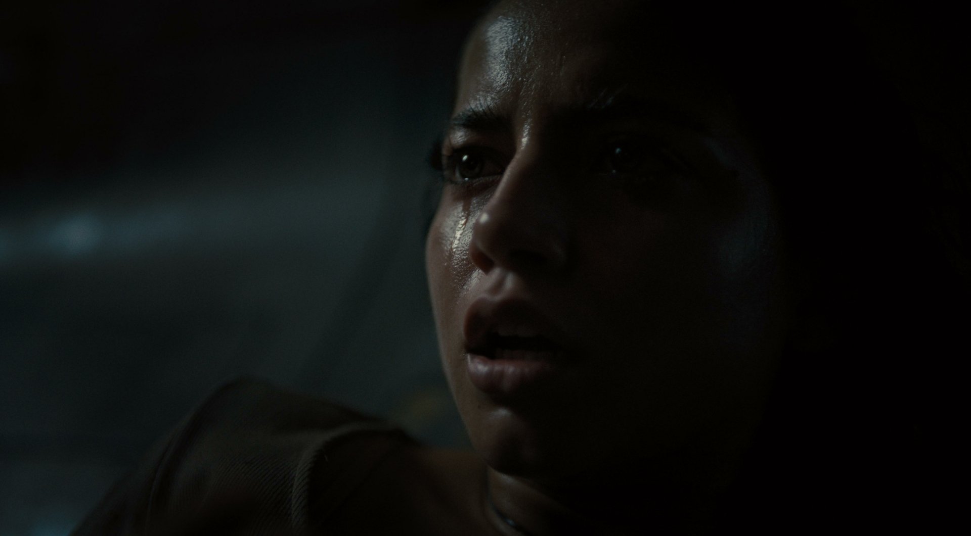 A close-up of Isabela Merced from the movie Alien: Romulus, capturing a tense moment with an intense expression, set against a dark and atmospheric backdrop.