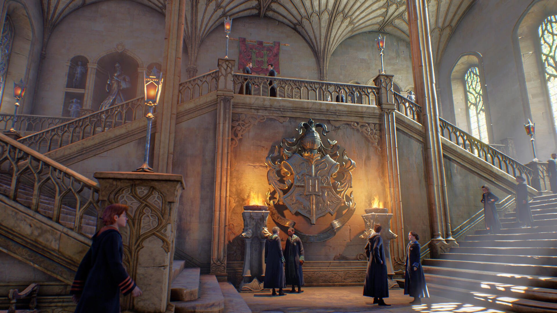 Hogwarts Legacy 2K Quad HD PC desktop wallpaper and background: robed students stand in a sunlit castle stairhall beneath a glowing house crest, arched stone ceiling and stained-glass windows.