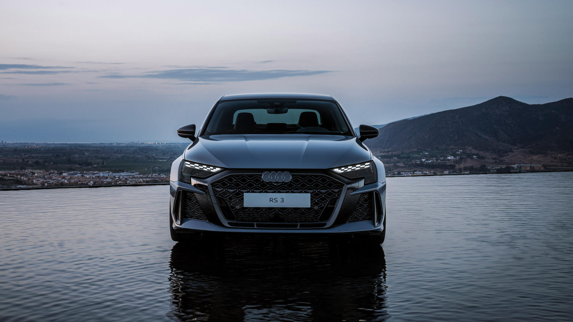 A stunning Audi RS3 Sedan stands poised against a serene backdrop, reflecting its sleek design and performance in this captivating 4K Ultra HD desktop wallpaper.