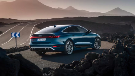 An Audi S6 E-Tron parked on a winding road, surrounded by mountains, showcasing its sleek design against a dramatic landscape. High-definition wallpaper background.