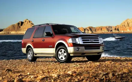 A Ford Expedition parked on a rocky shore, with a scenic background of water and rugged hills, captured in high-definition quality as a desktop wallpaper.
