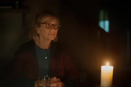 A woman with glasses sits in dim light, focused on a flickering candle, capturing a moment of introspection from the TV show Teacup (2024). 4K Ultra HD wallpaper background.