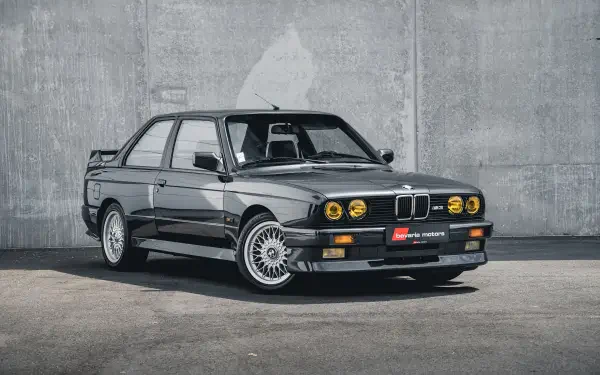 HD PC desktop wallpaper featuring a sleek black BMW E30 M3 parked against a concrete wall, highlighting its classic design and iconic status.