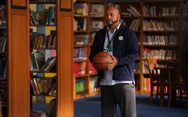 A scene from the TV show *Abbott Elementary*, featuring a character holding a basketball in a library filled with books, creating a vibrant educational atmosphere.
