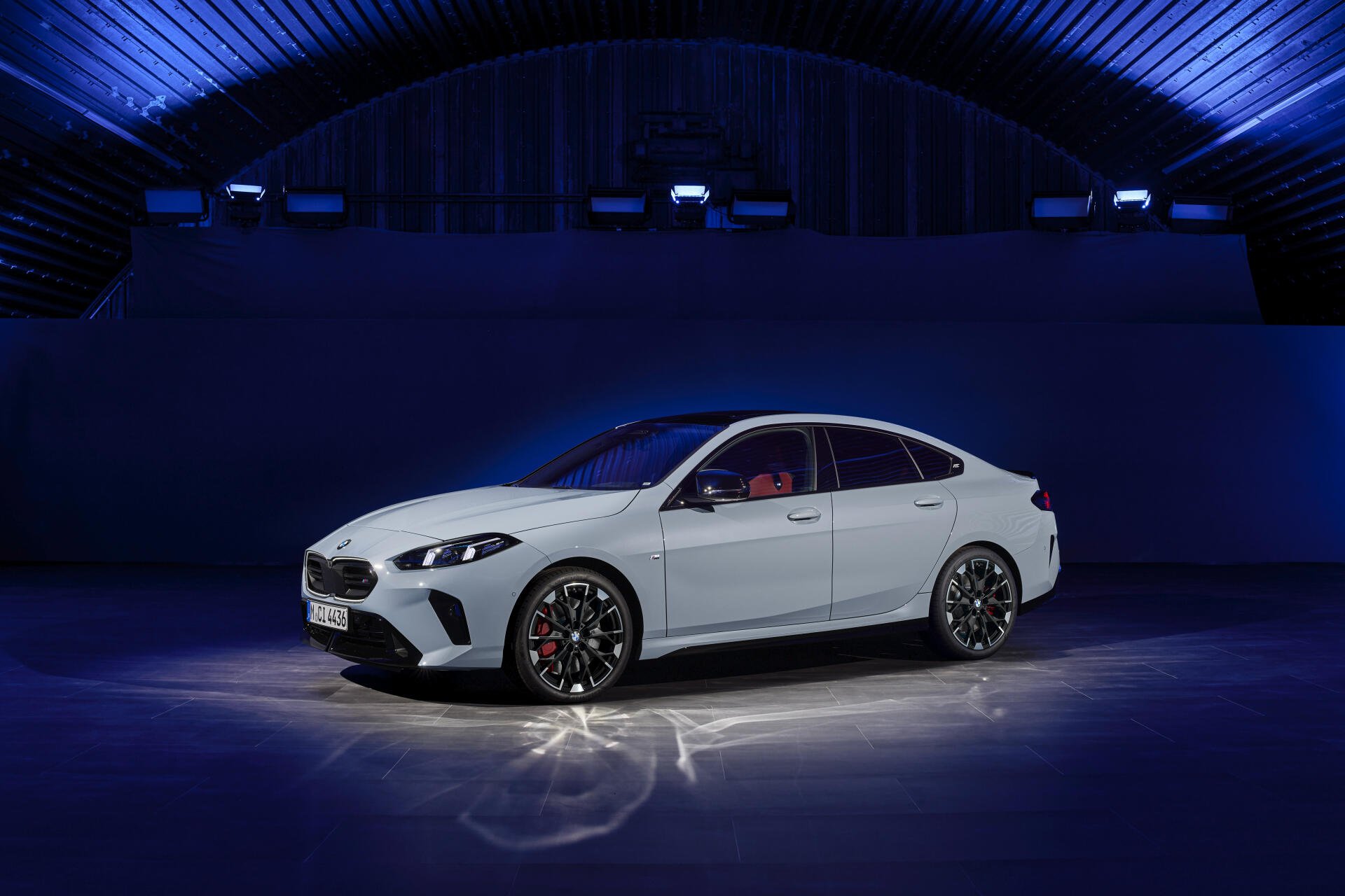 A sleek BMW M235 xDrive Gran Coupe showcased in a modern setting, featuring a striking white exterior and stylish alloy wheels, illuminated under dynamic blue lighting.