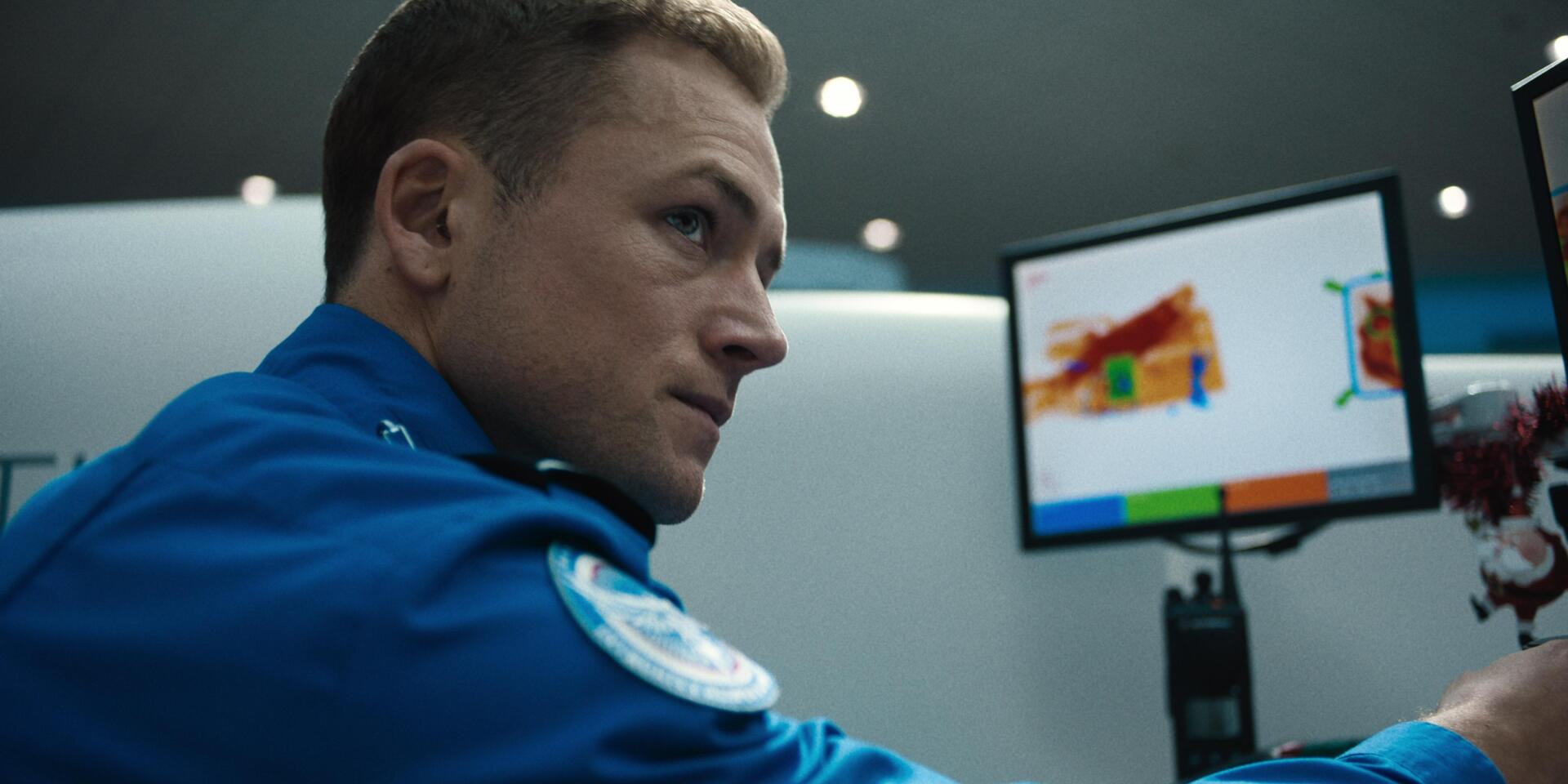 Taron Egerton in a scene from the movie Carry On (2024), portrayed against a backdrop featuring a high-tech screening monitor. 4K Ultra HD wallpaper.