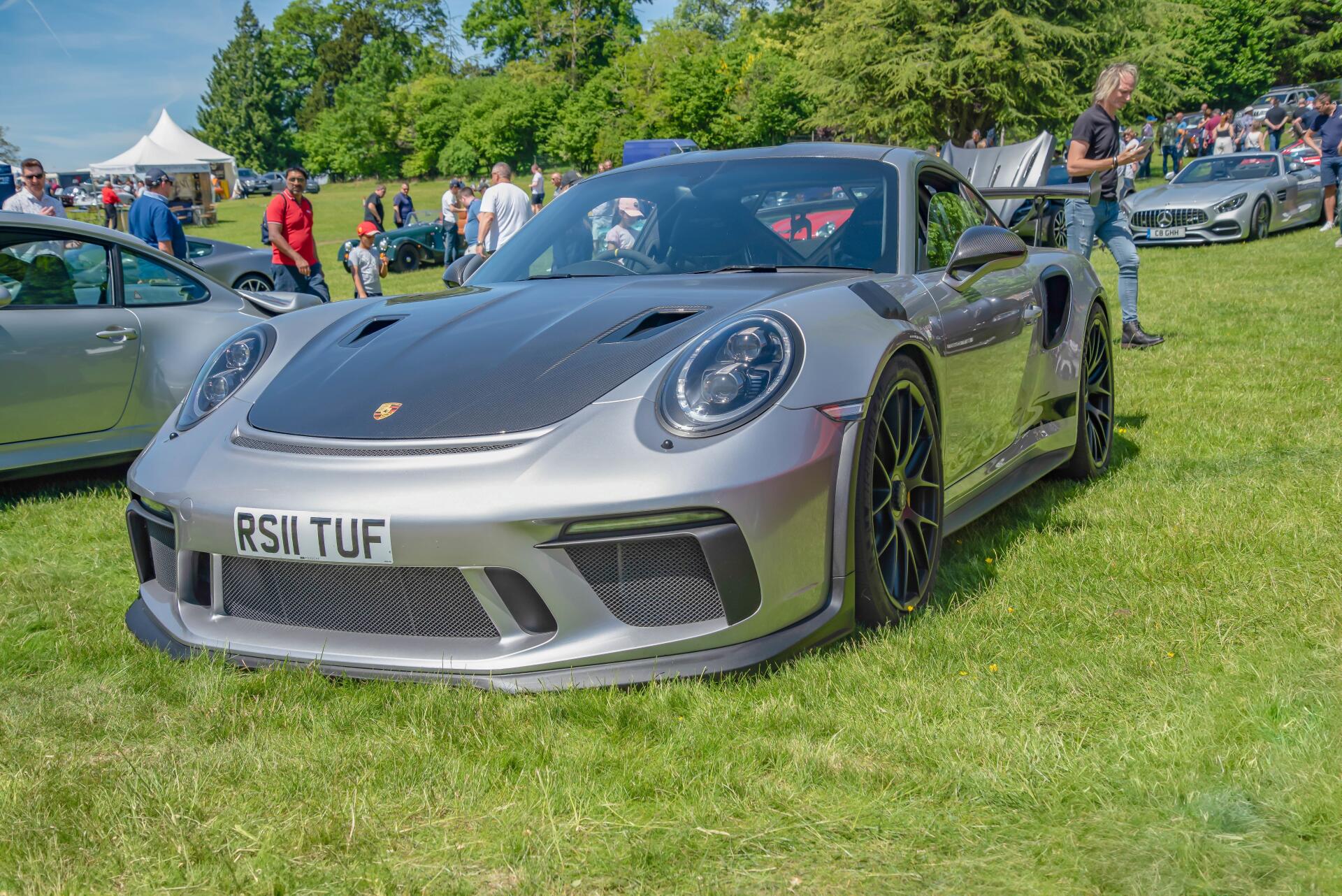 Silver Porsche sports car parked on grass at a car show, front three-quarter view with crowd in background — 5K Ultra HD PC desktop wallpaper and background.