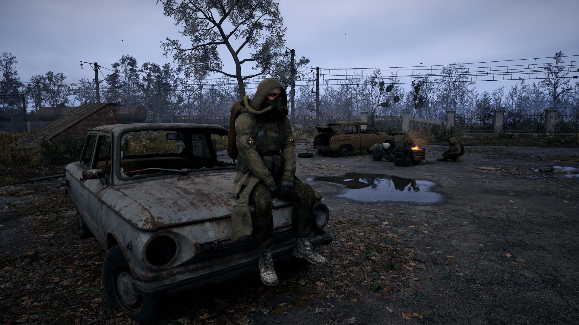 A character in a tattered suit sits on a rusted car in a desolate landscape, evoking the atmosphere of S.T.A.L.K.E.R. 2: Heart of Chernobyl in this HD PC desktop wallpaper.