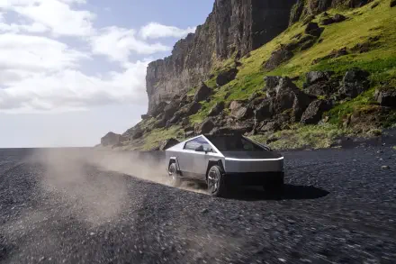 A Tesla Cybertruck drives along a rugged, dusty path beside a striking cliff, showcasing its futuristic design against a scenic landscape in this 4K Ultra HD wallpaper.