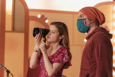 A scene from Woman of the Hour featuring Anna Kendrick holding a camera, capturing a moment alongside a masked companion. An 8K Ultra HD PC desktop wallpaper.