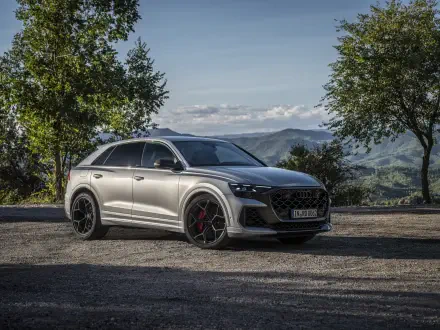 A sleek Audi RS Q8 parked on a scenic gravel road, surrounded by lush greenery and mountains, showcased in stunning 4K Ultra HD quality.