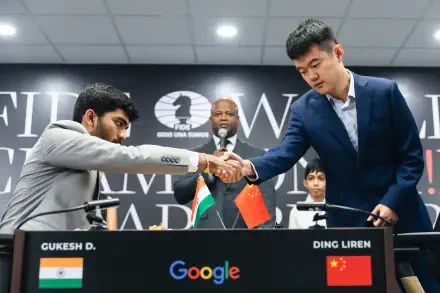 Gukesh Dommaraju and Ding Liren shake hands before their match at the World Chess Championship, with a backdrop featuring national flags and a Google logo.