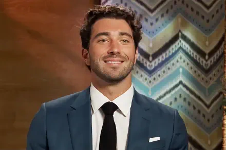 A confident Joey Graziadei poses in a sharp suit against a vibrant patterned backdrop, making for an engaging HD PC desktop wallpaper and background.