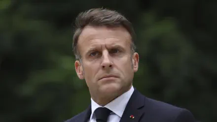 A high-definition desktop wallpaper of Emmanuel Macron, featuring him with a serious expression against a blurred natural background.