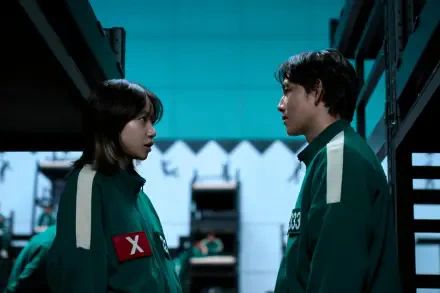 A scene from the TV show Squid Game, featuring two characters in green uniforms, facing each other amidst a stark, industrial backdrop, creating an intense atmosphere. HD PC desktop wallpaper.
