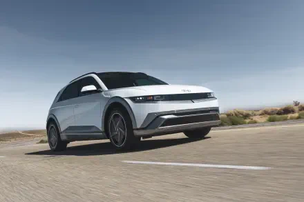 A sleek Hyundai IONIQ 5 drives along a deserted road under a clear blue sky, showcasing its modern design. This stunning 4K Ultra HD wallpaper highlights the car's features beautifully.