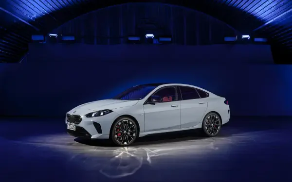A sleek BMW M235 xDrive Gran Coupe showcased in a modern setting, featuring a striking white exterior and stylish alloy wheels, illuminated under dynamic blue lighting.