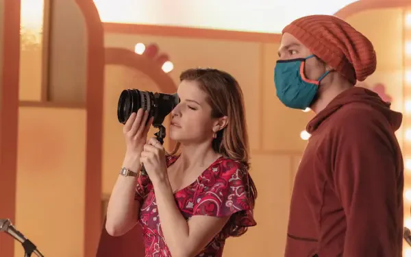 A scene from Woman of the Hour featuring Anna Kendrick holding a camera, capturing a moment alongside a masked companion. An 8K Ultra HD PC desktop wallpaper.