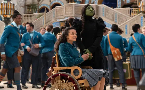 A vibrant scene from the movie *Wicked*, featuring Cynthia Erivo in character alongside a seated companion, with a lively crowd in colorful costumes in the background.