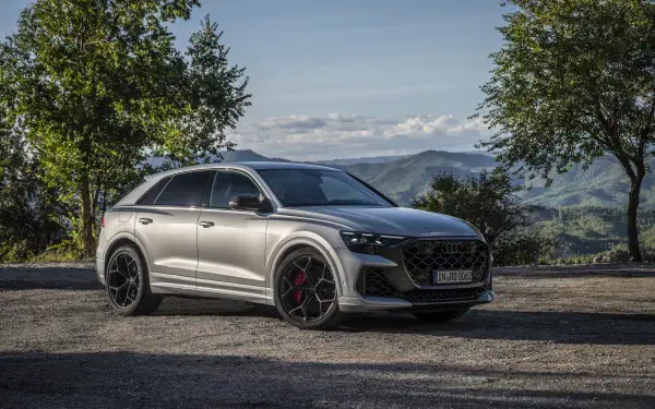 A sleek Audi RS Q8 parked on a scenic gravel road, surrounded by lush greenery and mountains, showcased in stunning 4K Ultra HD quality.
