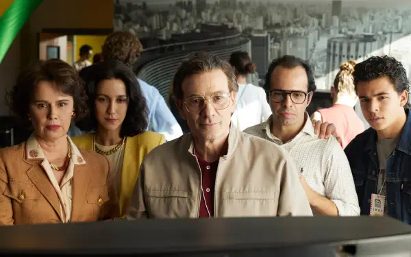 A gripping scene from the TV show Senna (2024), featuring five characters intently focused on a monitor, set against a backdrop of a bustling cityscape. 4K Ultra HD wallpaper and background.